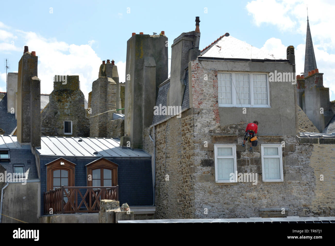 Muratore rappeling da un tetto ed intonaci di facciata nella città vecchia, Francia Bretagna, Saint-Malo Foto Stock