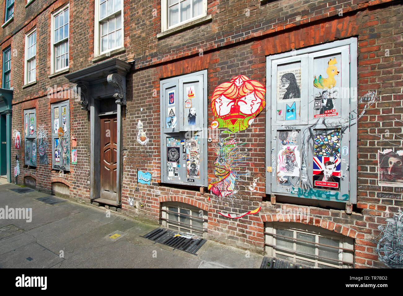 Londra SPITALFIELDS BRICK LANE GAFFITI intelligente e l'arte al muro con case di mattoni e una vecchia porta di legno Foto Stock