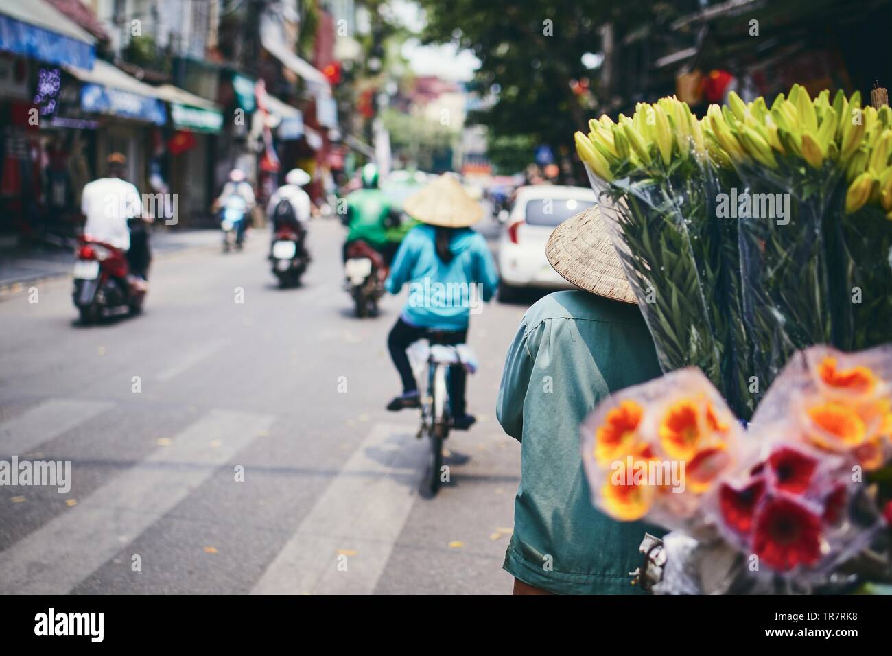 La vita della città in strada del quartiere vecchio di Hanoi. Venditore di fiori nel tradizionale cappello conico, Vietnam. Foto Stock