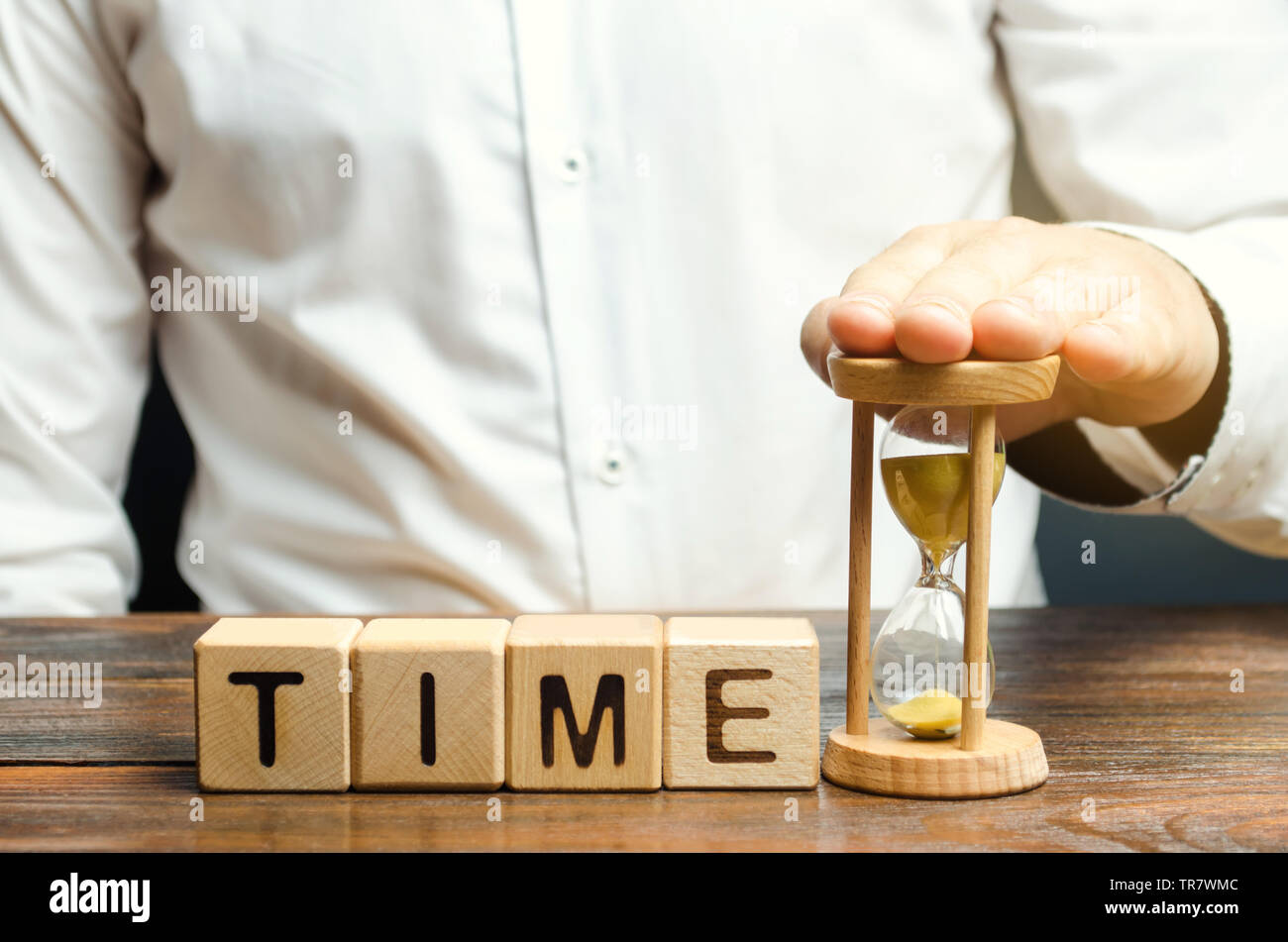 Un uomo mette la clessidra vicino a dei blocchi di legno con il tempo di parola. Concetto di gestione del tempo e la distribuzione corretta. Attività di pianificazione e di lavoro. Business y Foto Stock