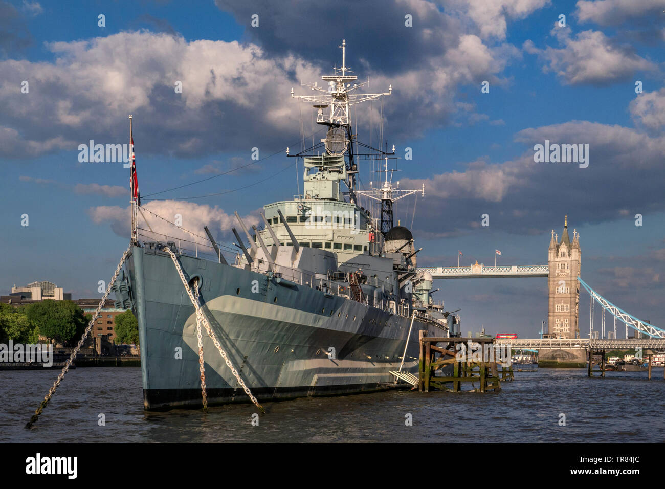 HMS Belfast attrazione turistica nave, ormeggiato sul fiume Tamigi nel tardo pomeriggio la luce del sole, con il Tower Bridge e London bus rosso che attraversa Londra SE1 Foto Stock