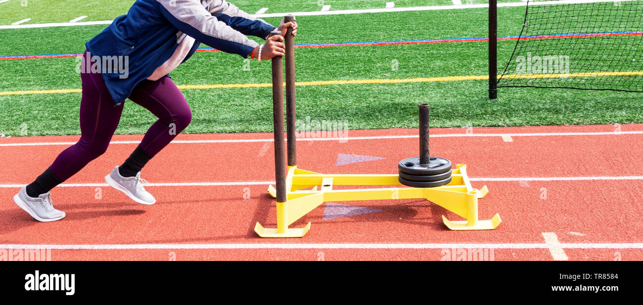 Una scuola di colpo messo ragazza sta spingendo una slitta di giallo con settanta cinque libbre di peso su di esso verso il basso una pista rossa. Foto Stock