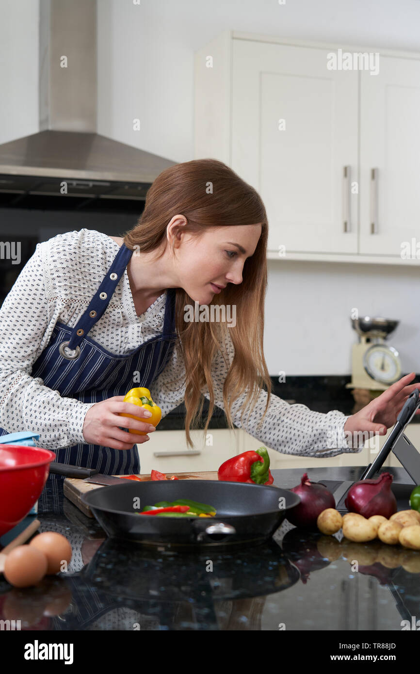 La donna in cucina a casa ricetta seguente sulla tavoletta digitale Foto Stock