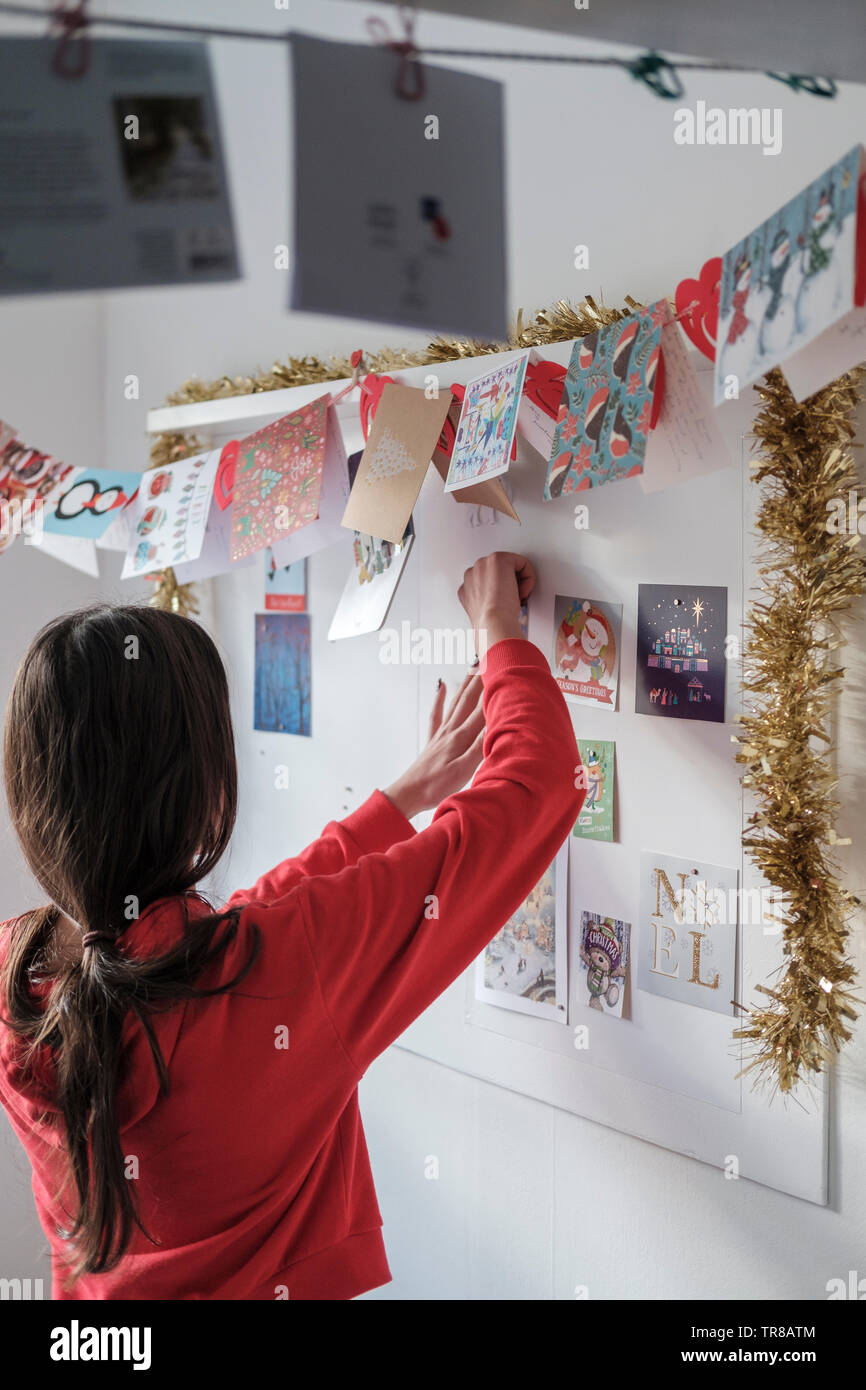 Ragazza adolescente appendere le carte di Natale a casa Foto Stock