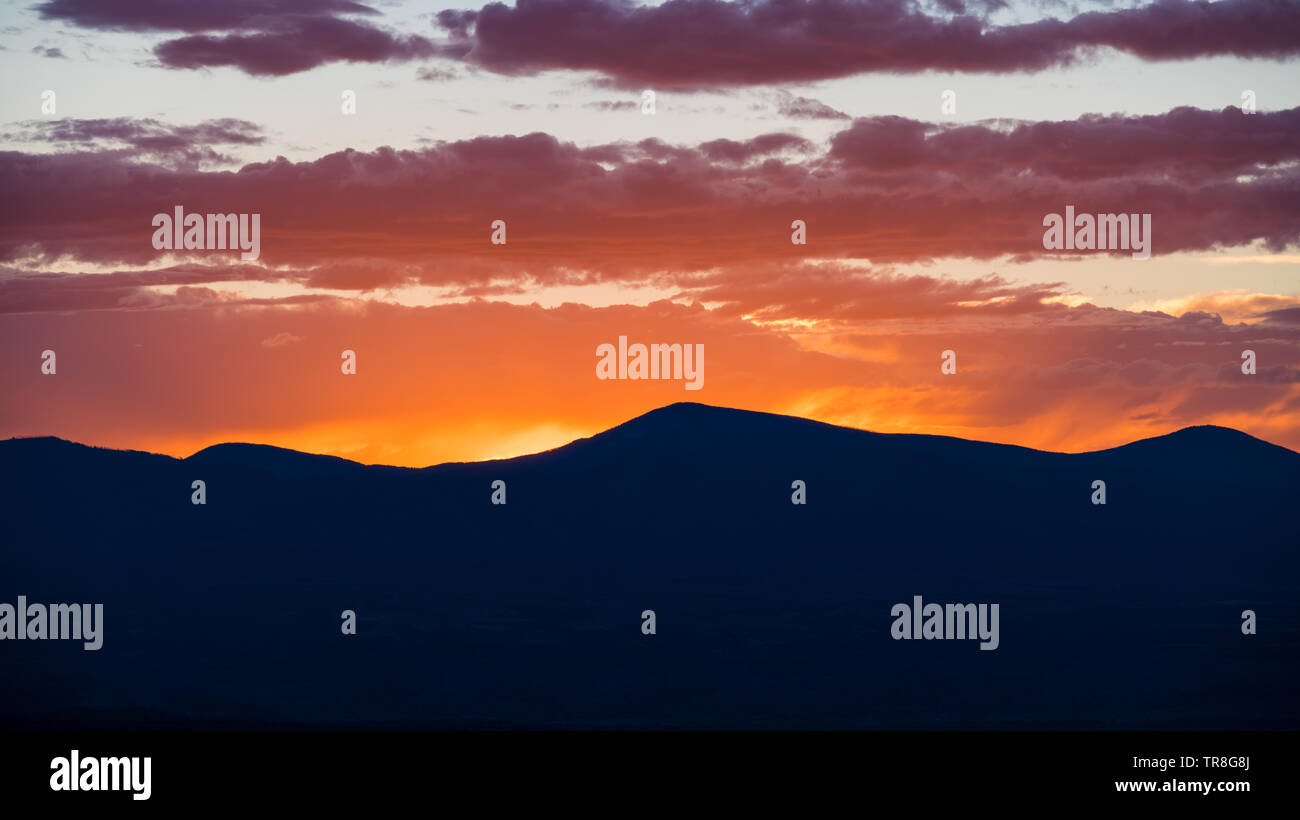 Sunset silhouettes una gamma della montagna e i colori del cielo e delle nubi in giallo, arancione, viola e rosa - Jemez montagne vicino a Santa Fe, New Mexico Foto Stock
