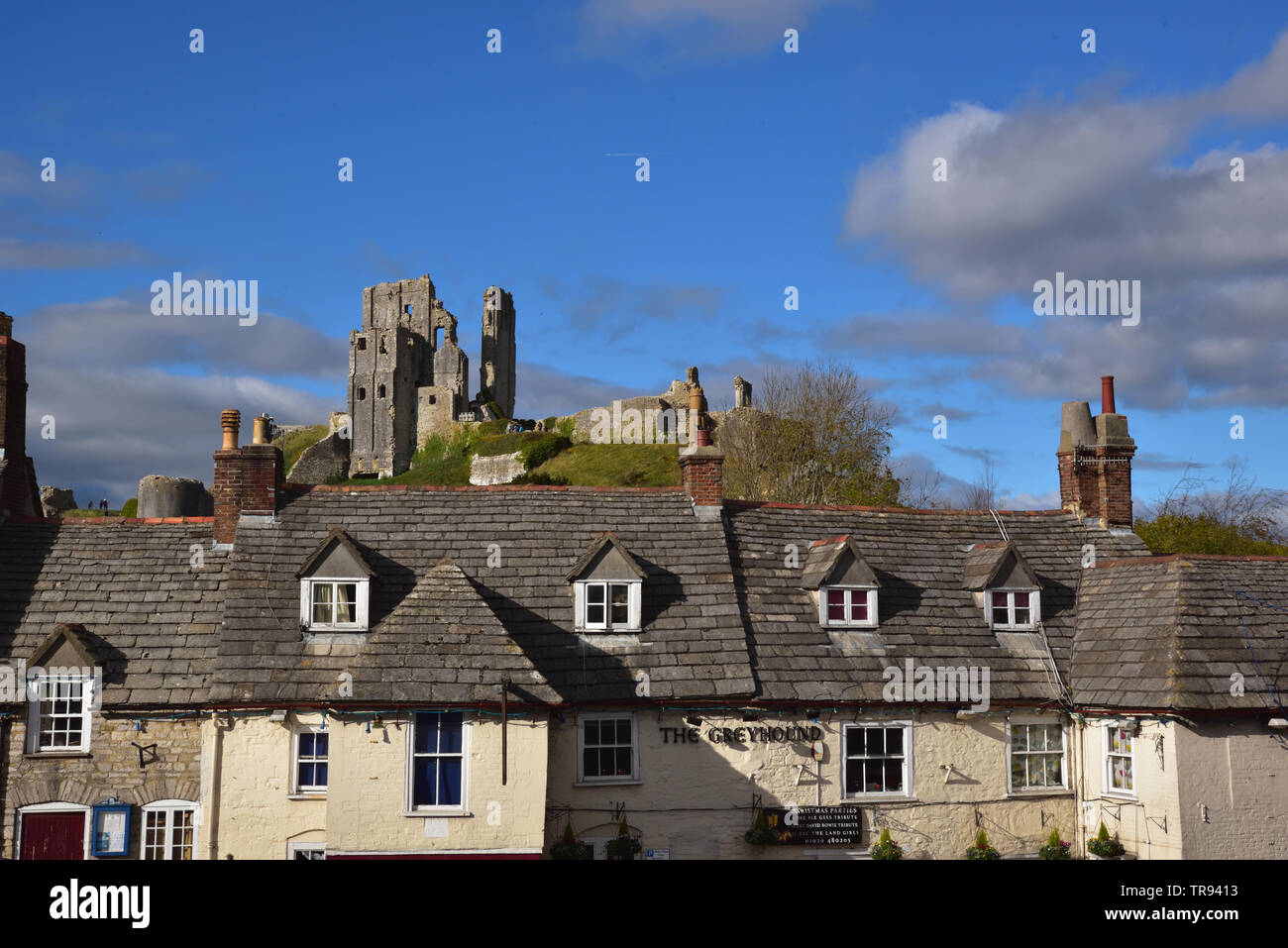 Le rovine di Corfe Castle appollaiato sulla cima di una collina dietro il pub Greyhound. Foto Stock