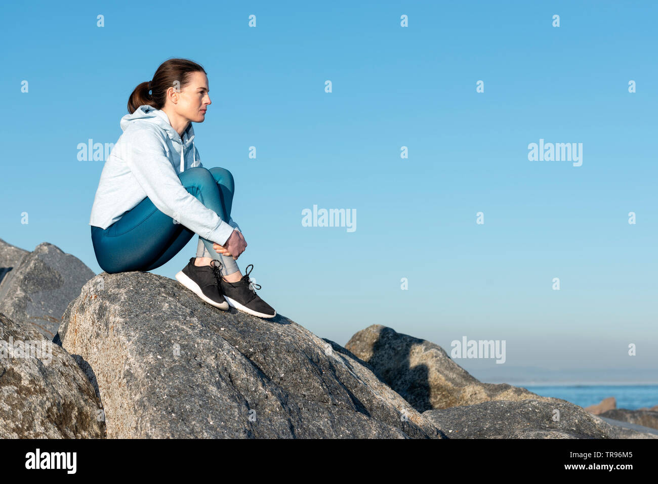 Donna seduta sulla sommità di massi di pensare, cielo blu sullo sfondo. Foto Stock
