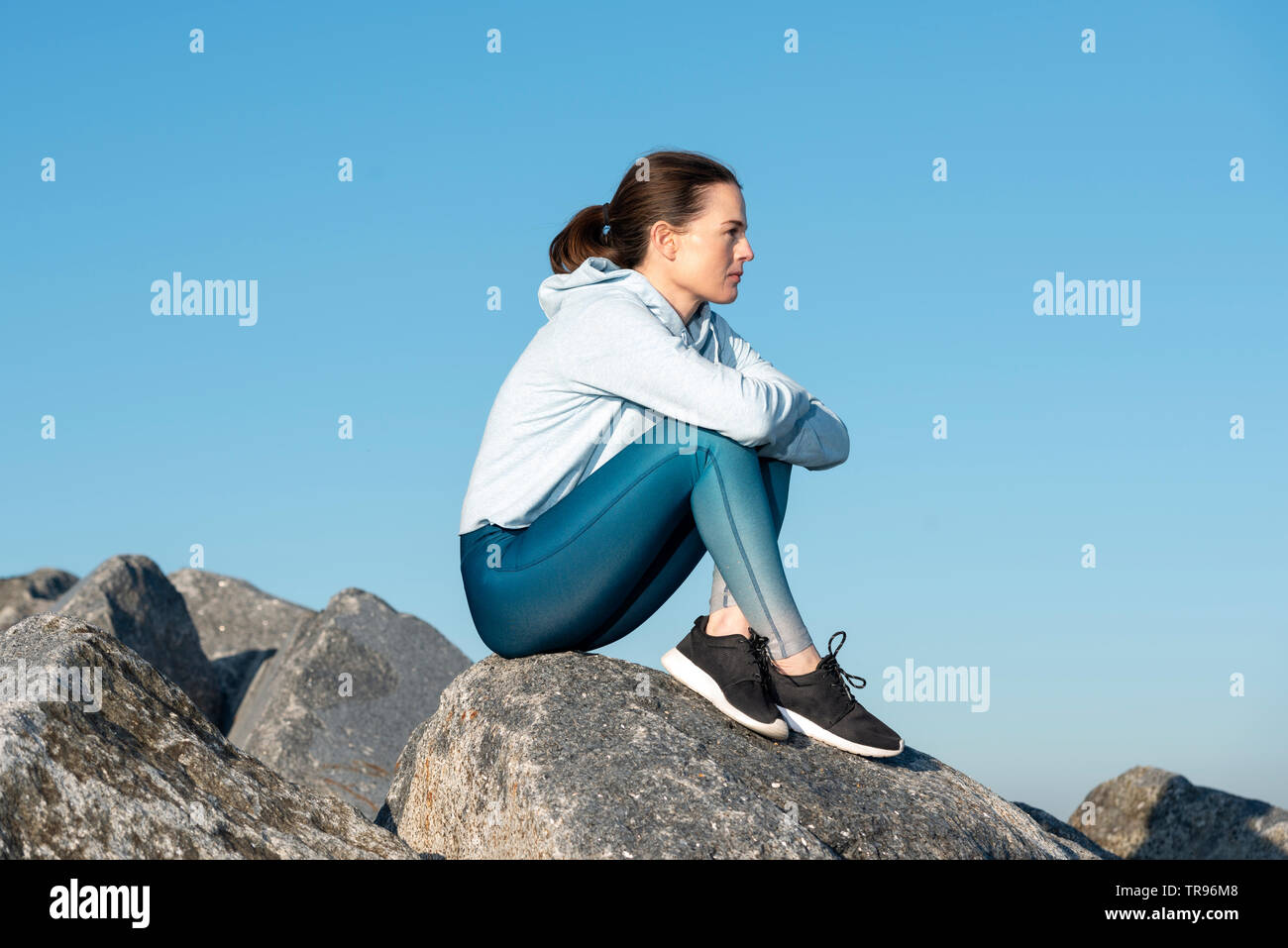 Donna seduta sulla sommità di massi di pensare, cielo blu sullo sfondo. Foto Stock