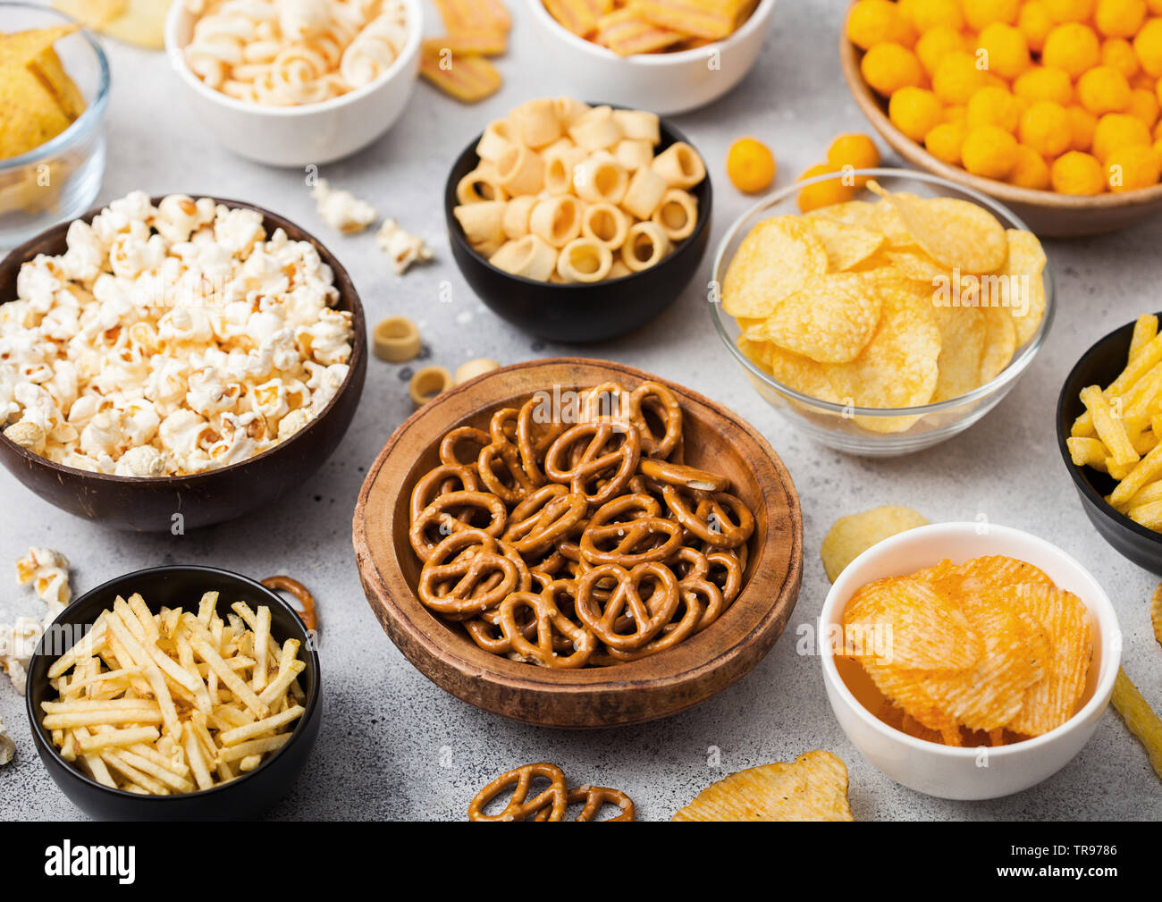 Tutti i classici snack di patate con arachidi, popcorn e anelli di cipolla e salati pretzel nel recipiente delle piastre sul tavolo luminoso. Ghirigori con bastoni e patatine fritte Foto Stock