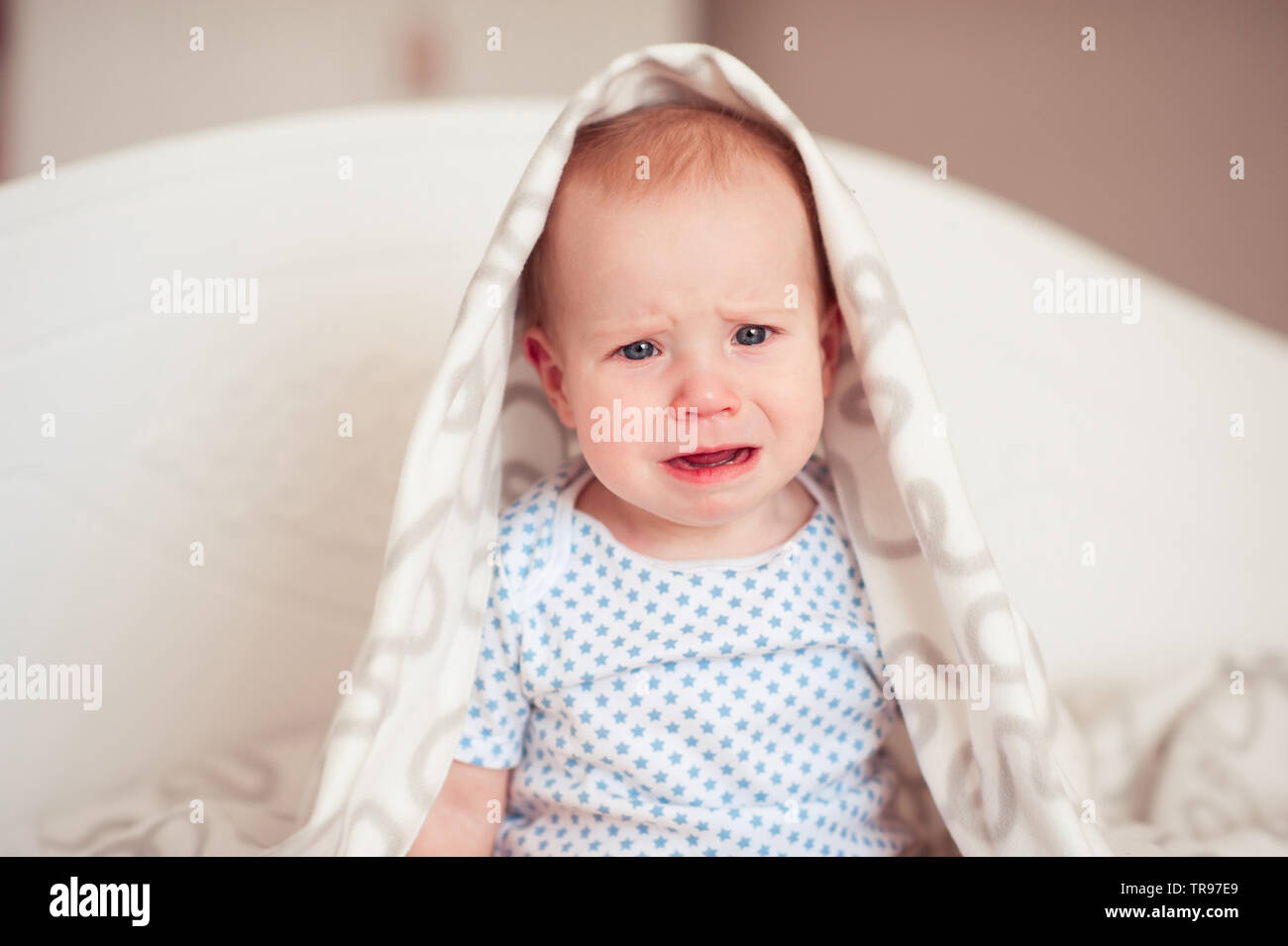 Il pianto baby boy 8-9 mesi seduta nel letto guardando la fotocamera. La tristezza. Infanzia. Foto Stock