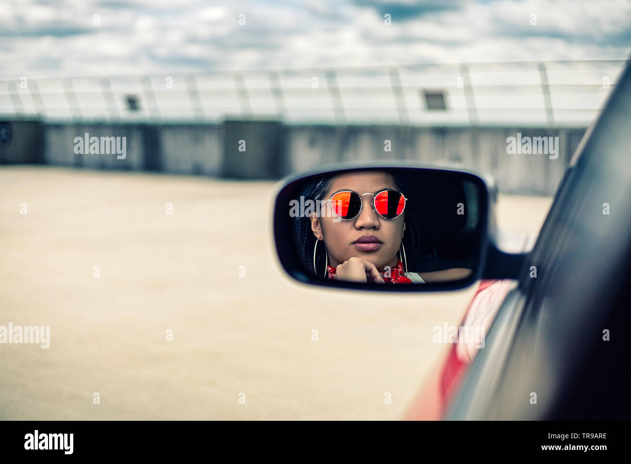 Donna asiatica indossando occhiali da sole cercando nella vista posteriore della sua Dodge Charger auto Foto Stock