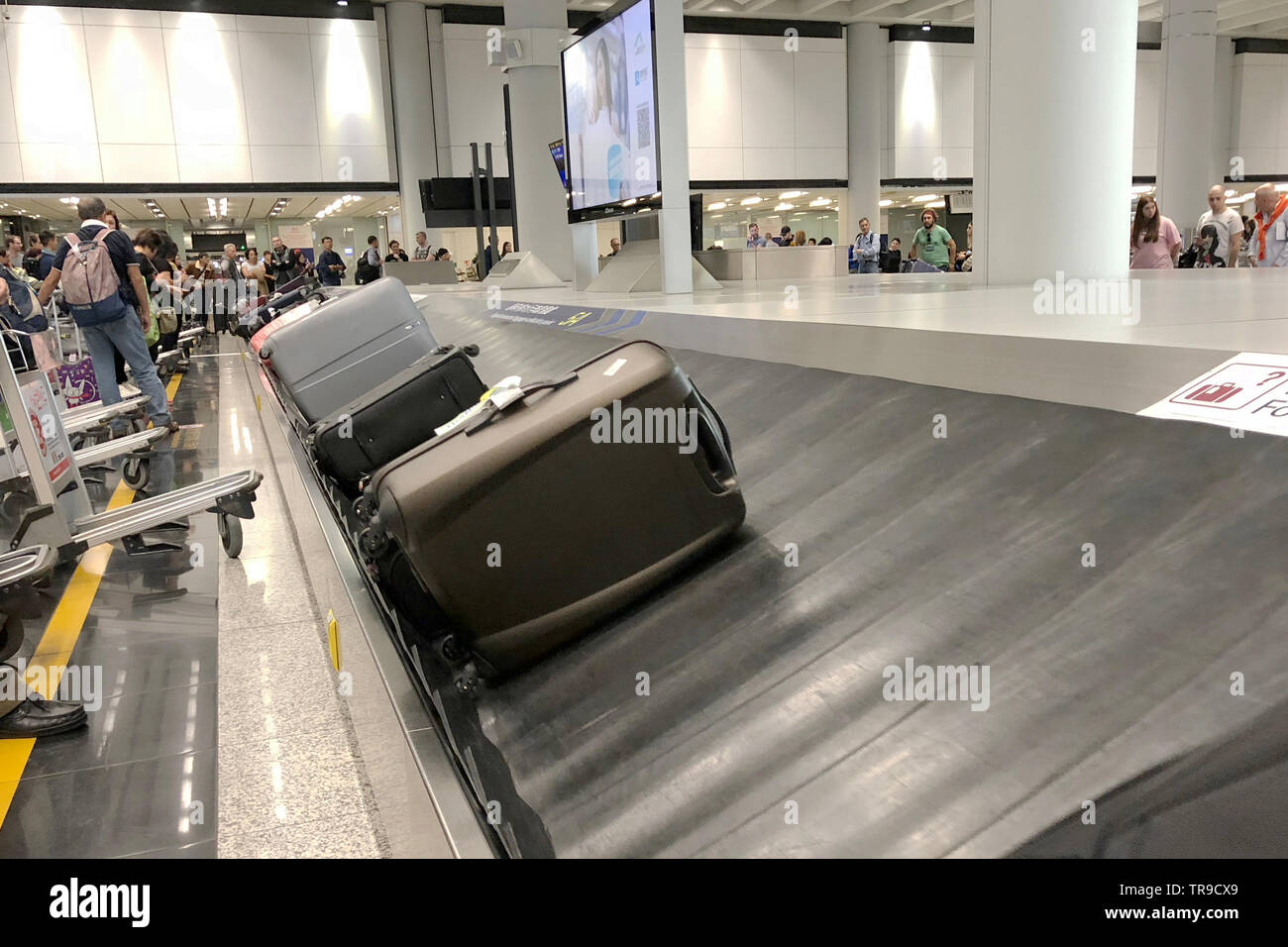 Bagagli nastro trasportatore con valigie personali muoversi in cerchio. Multirazziale persone in attesa per i loro bagagli. L'Aeroporto Internazionale di Hong Kong. Foto Stock