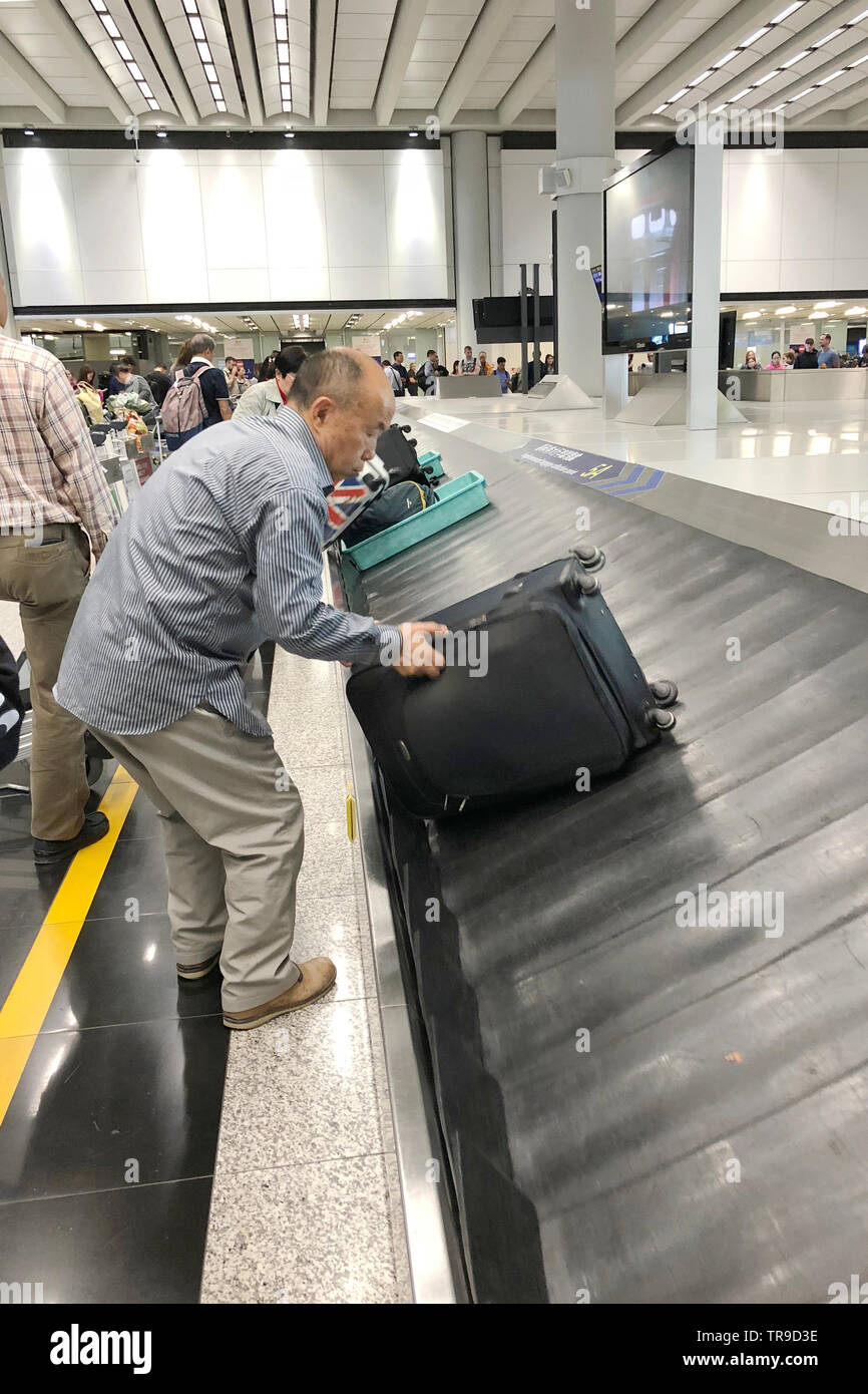 Bagagli nastro trasportatore con valigie personali muoversi in cerchio. Multirazziale persone in attesa per i loro bagagli. L'Aeroporto Internazionale di Hong Kong. Foto Stock