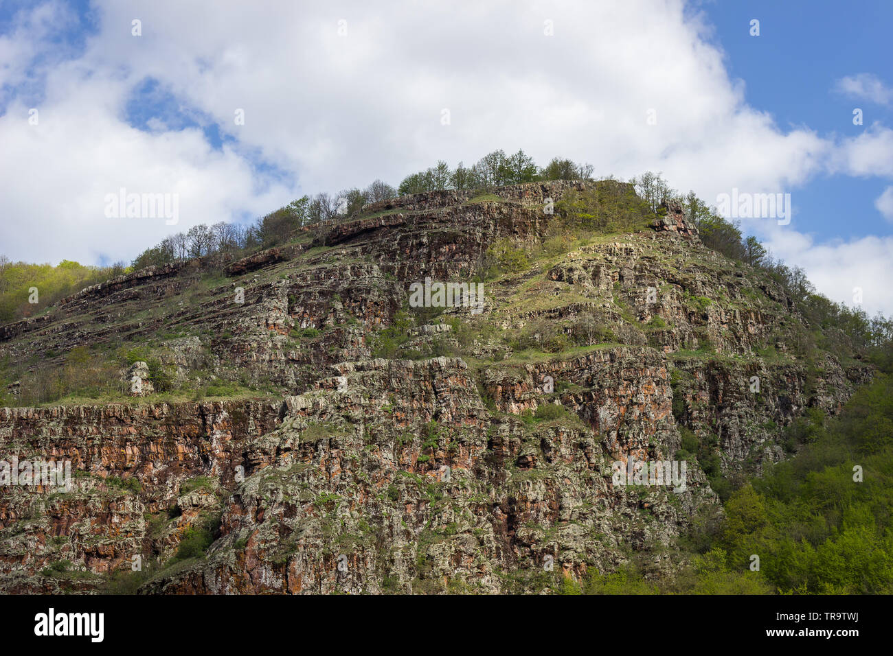 Impressionante, rosso, picco roccioso sulla vecchia montagna (Stara Planina) in Serbia, coperti dal verde vivace, soleggiato alberi e cespugli in primavera Foto Stock