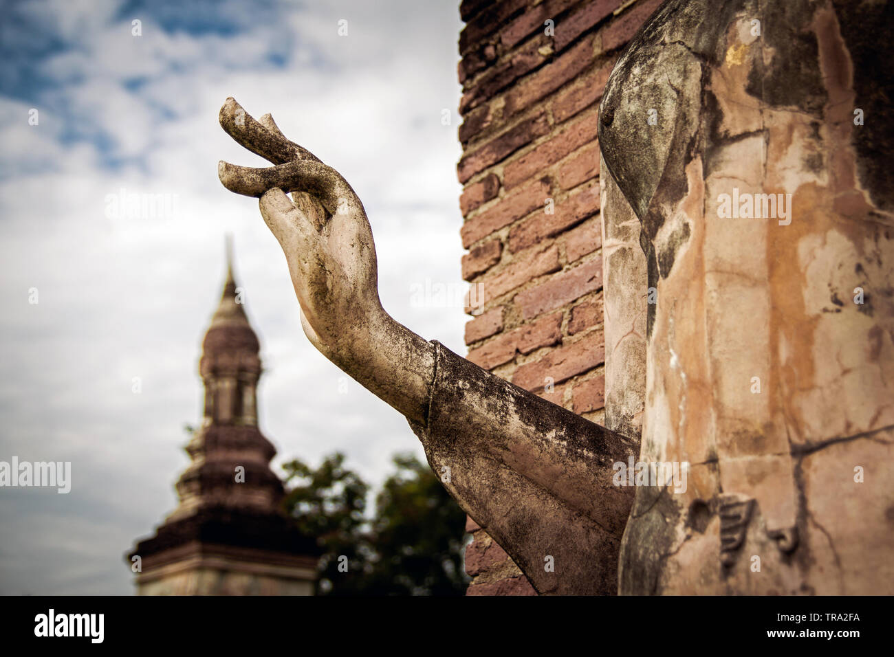 Statua di Buddha in Sukhothai parco storico con le dita in spirituale mudra gesto apparentemente toccando la guglia di un antico stupa in background Foto Stock
