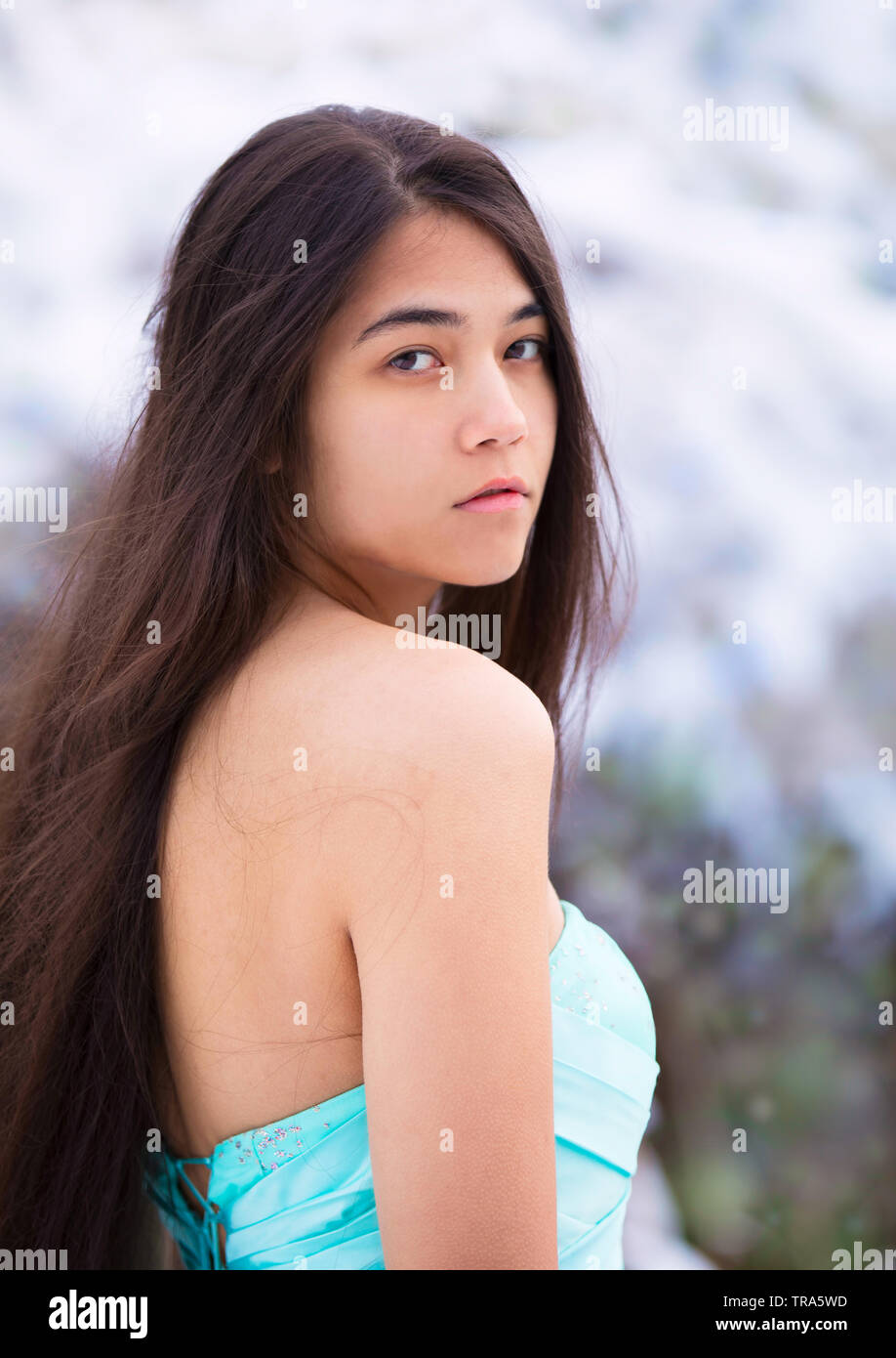 Biracial teen ragazza o giovane donna di asiatici e caucasici indossando la discesa vestito blu all'aperto nella neve guardando sopra la spalla in telecamera Foto Stock