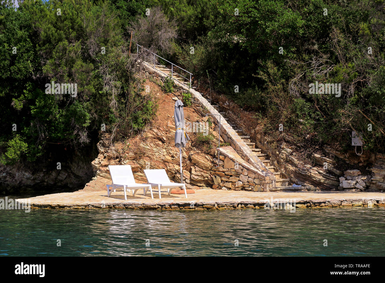 Spiagge private sul mare mediterraneo. Sedie, sdraio, ombrelloni e sedie a sdraio in attesa per i turisti. Tiny appartata spiaggia rocciosa. Foto Stock