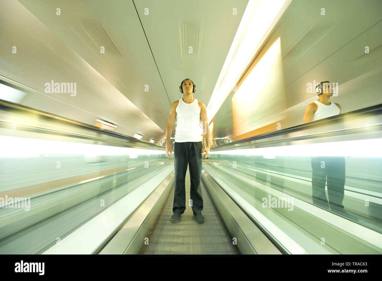 Amazing shot di un uomo moderno in piedi su una scala mobile in movimento che indossa le cuffie e ascolto di musica Foto Stock