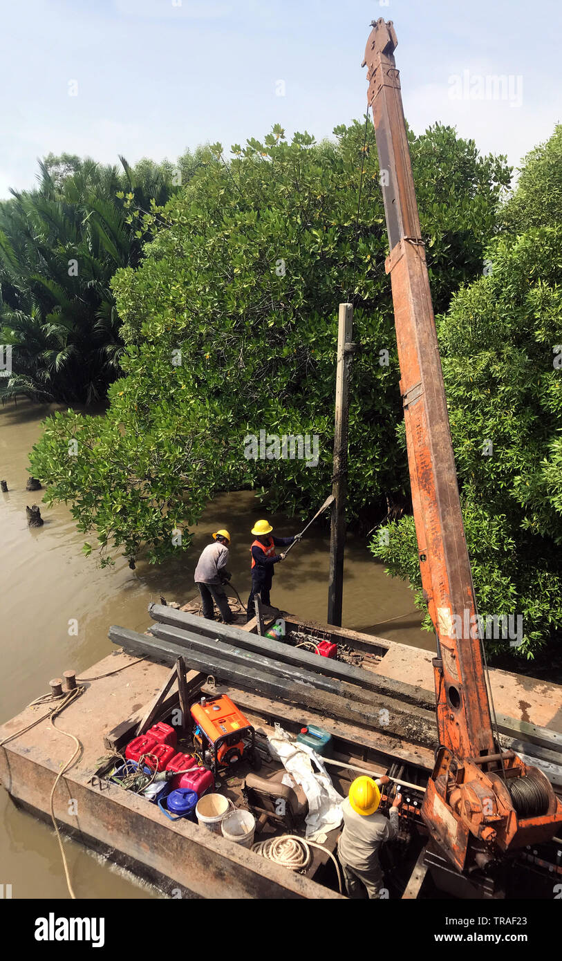 Team di collaboratori tirare le colonne di cemento al di fuori dell'acqua sul pontile di ferro con la gru. River Coast ricostruzione, Thailandia Foto Stock