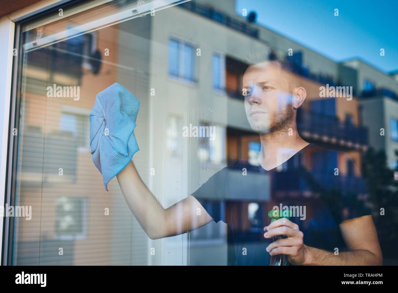 Uomo finestra di pulizia con un panno e il detergente spray a casa. Temi per i lavori domestici e il servizio di pulizie. Foto Stock