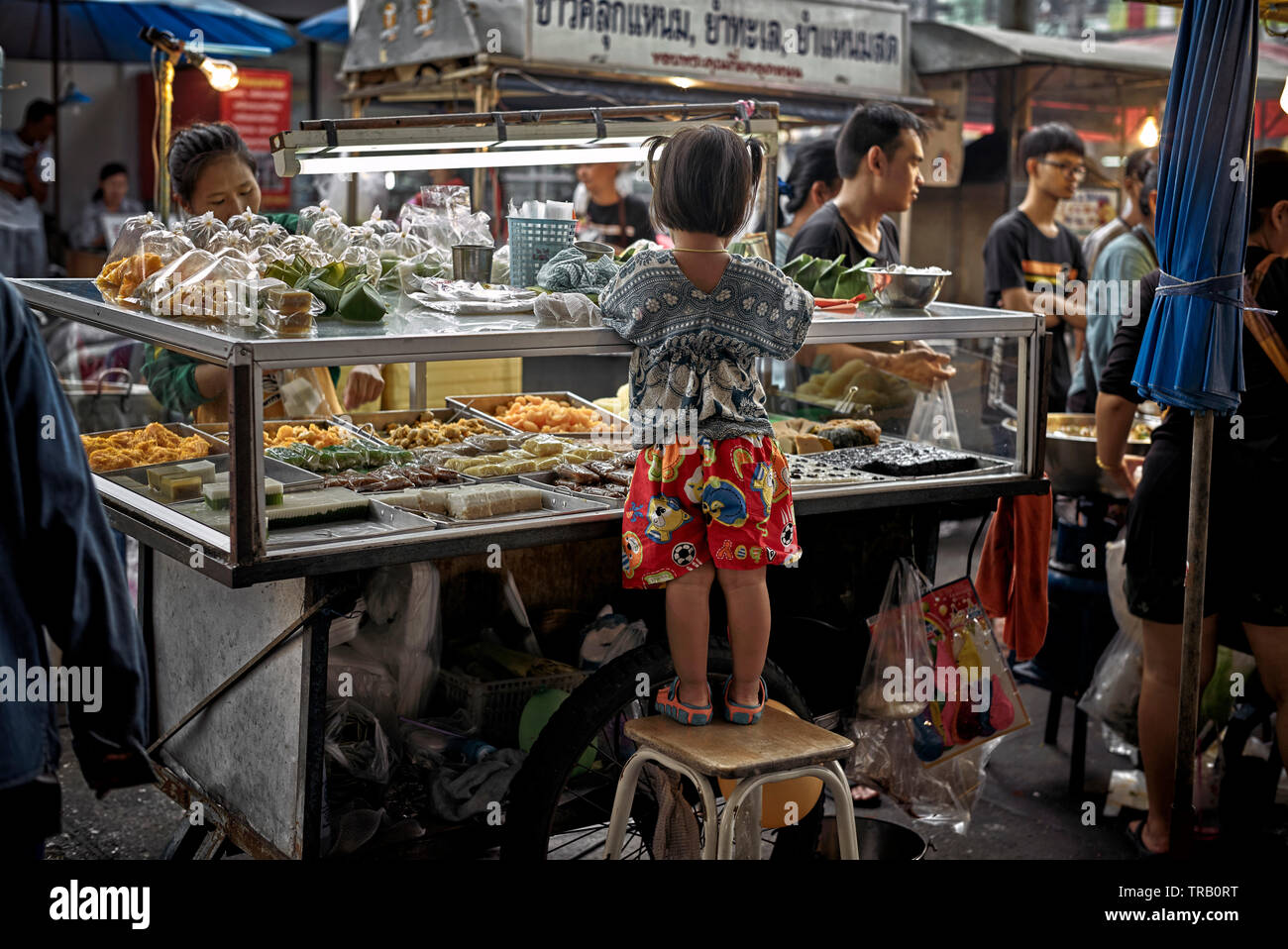 Bambino aiutando la madre a loro street market alimentare stallo. Della Thailandia Foto Stock