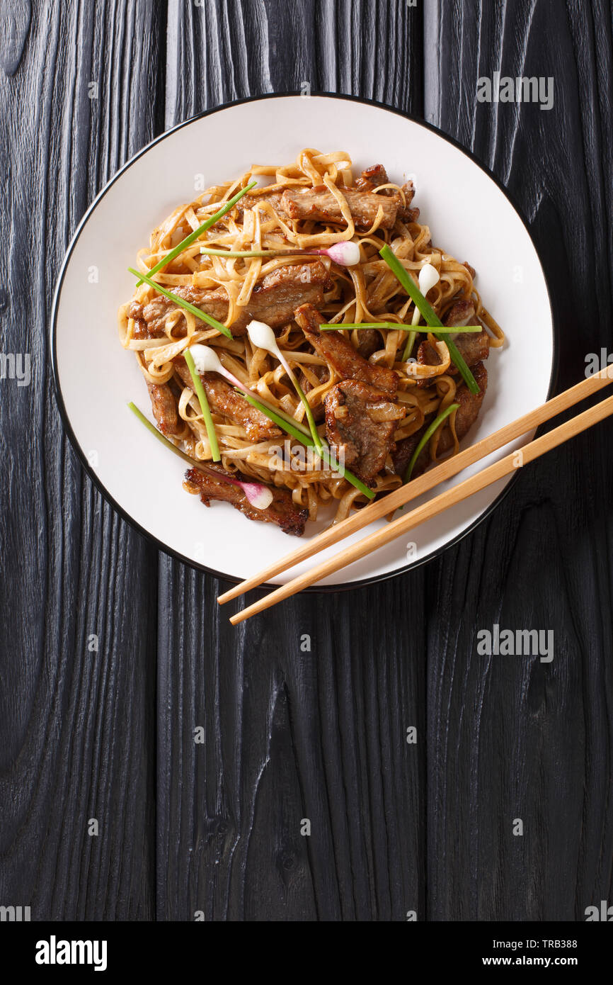 Carni bovine Chow Fun un fiocco piatto Cantonese, realizzato da friggere la carne bovina, ampia spaghetti di riso e verdure closeup sulla piastra della tavola di legno. In verticale Foto Stock