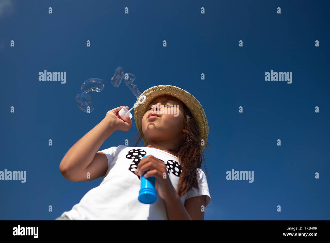 Amazing shot dinamico di una giovane ragazza asiatica che indossa un cappello di paglia a soffiare bolle in estate il sole al di fuori nelle dune Foto Stock
