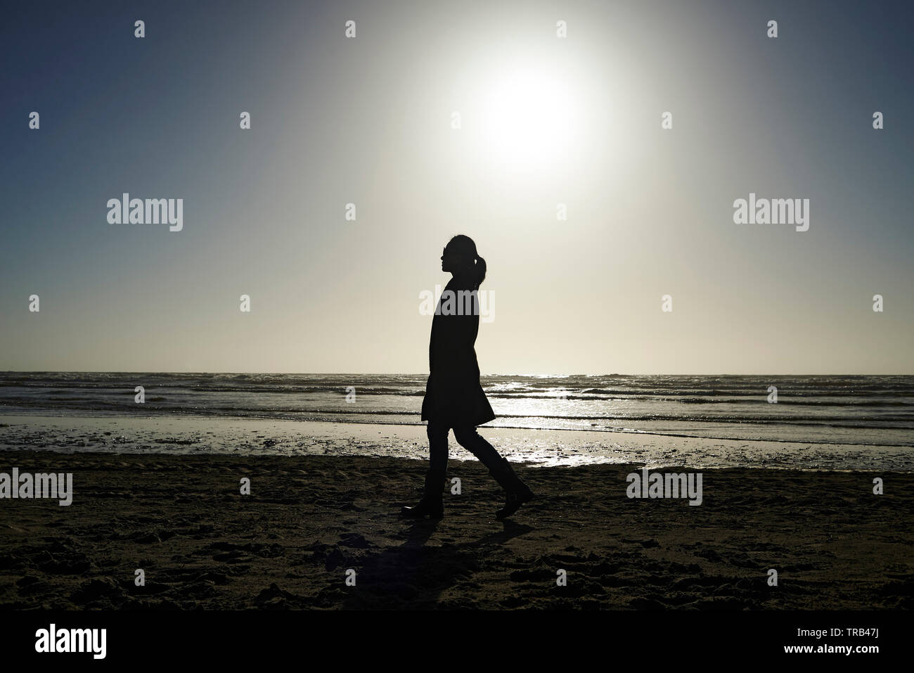 Profilo laterale sian donna nel pensiero profondo walkingalong la spiaggia in inverno il sole in pensiero profondo Foto Stock