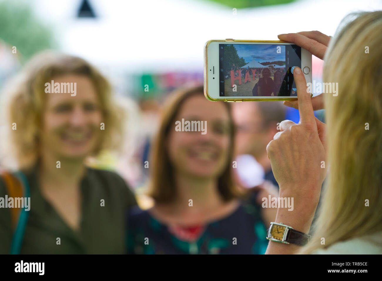Donna che utilizza iphone smartphone per la fotografia di due donne al Festival di Fieno Hay on Wye Powys Wales UK Foto Stock