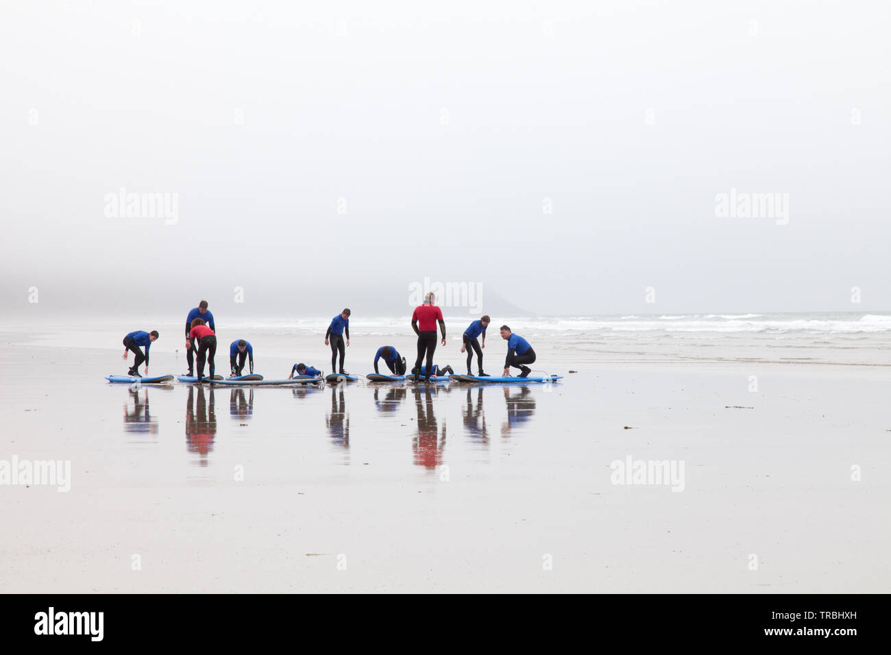 Spiaggia Newgale in Pembrokshire su un grigio e nebbioso giorno. Giovani studenti aventi la loro prima lezione di surf Foto Stock