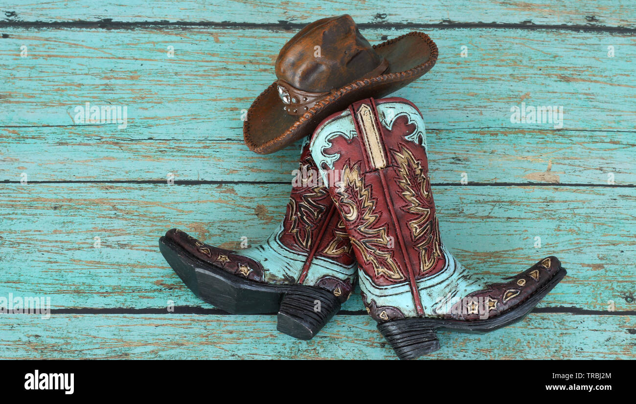Stivali da cowboy e cappello marrone e teal su uno sfondo in legno di teal Foto Stock