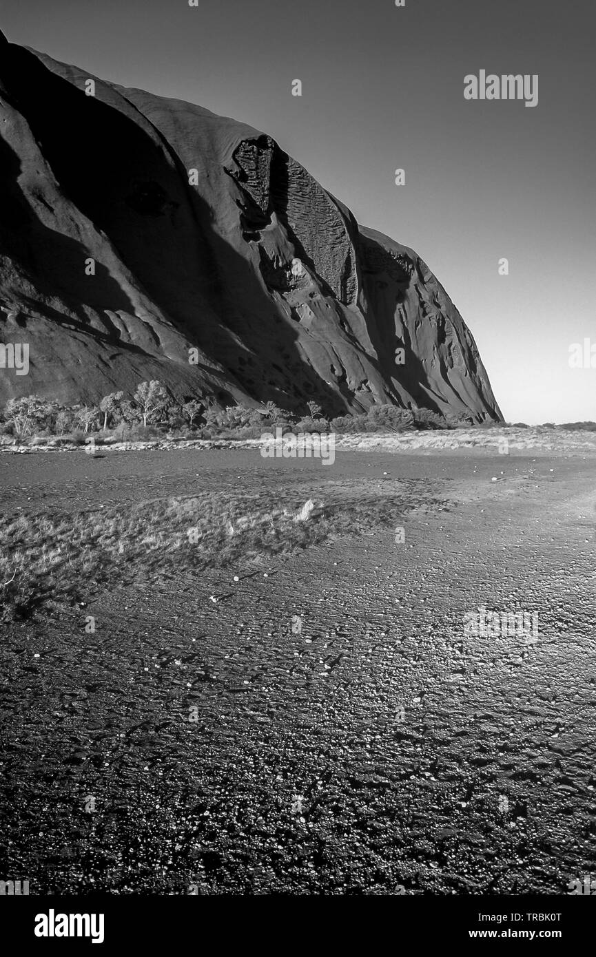 Il sole splende giù sul sentiero alla base del grande monolito Uluru (Ayers Rock) nel cuore dell'Australia Outback. Foto Stock