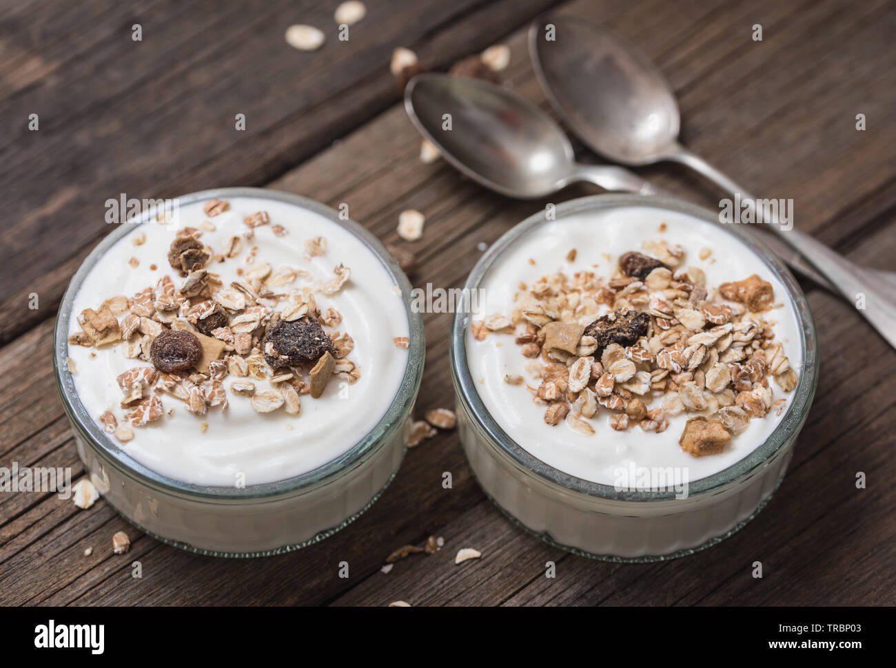 Due ciotole in vetro con yogurt bianco su una vecchia scrivania di legno con i fiocchi d'avena sulla parte superiore. Foto Stock