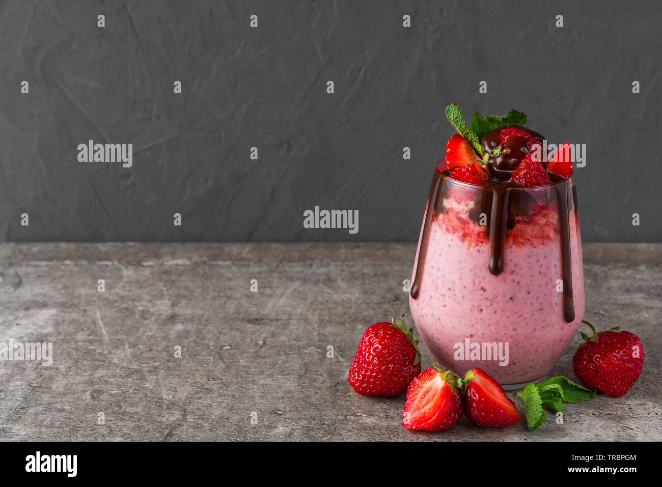 Fragola chia budino di sementi con cioccolato, frutti di bosco freschi e menta per una sana colazione gustosa su sfondo di calcestruzzo Foto Stock