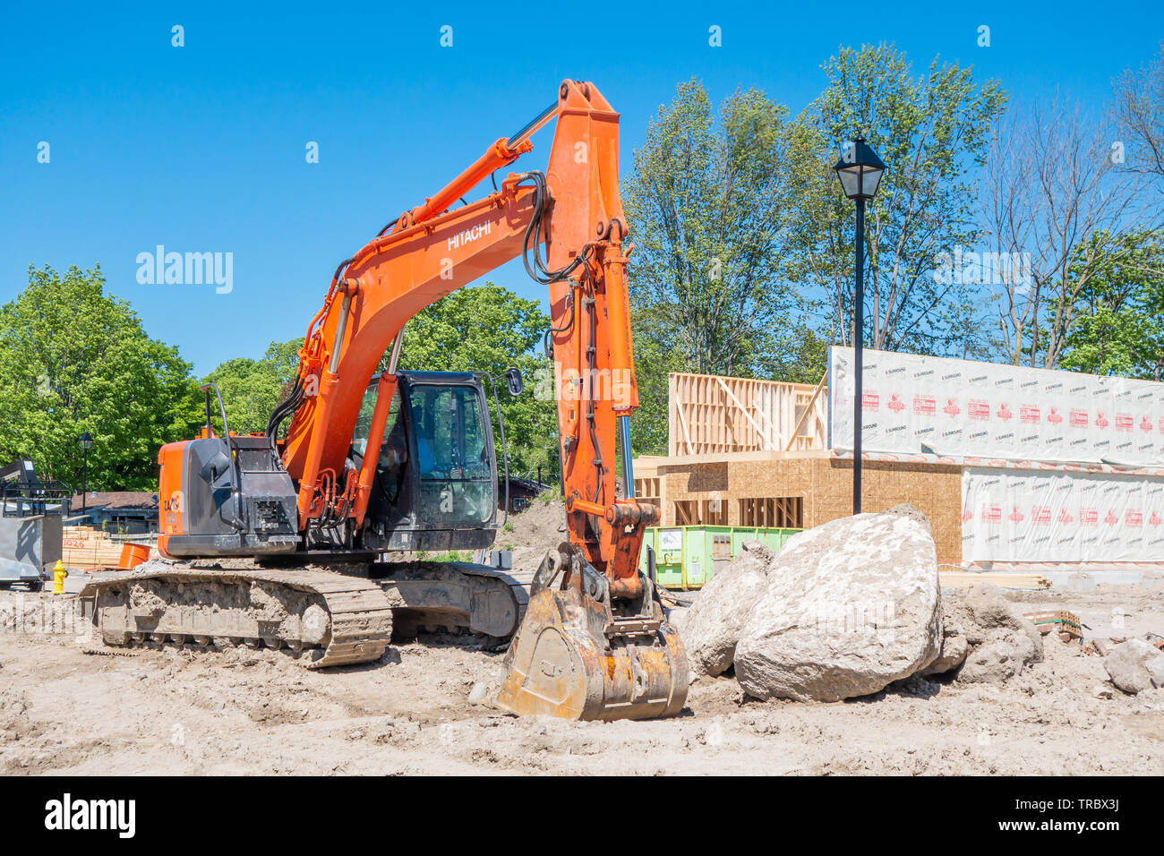 Escavatore si siede di fronte a una nuova casa in costruzione in una suddivisione di sviluppo. Foto Stock