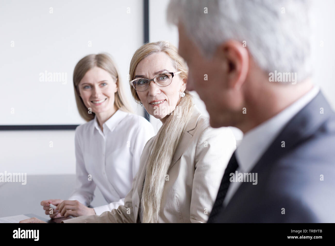 La gente di affari seduti in una fila e lavorare, concentrarsi sulla donna matura in bicchieri Foto Stock