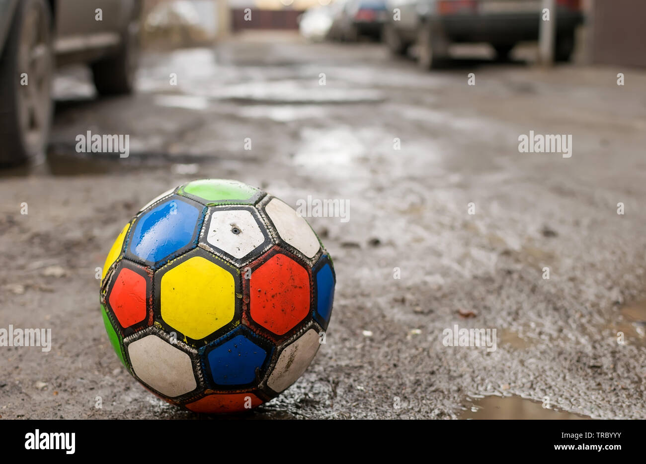 I bambini la palla calcio gioco è su una rotta sporca strada tra pozzanghere e cantieri residenziale di case, nei pressi di automobili parcheggiate Foto Stock
