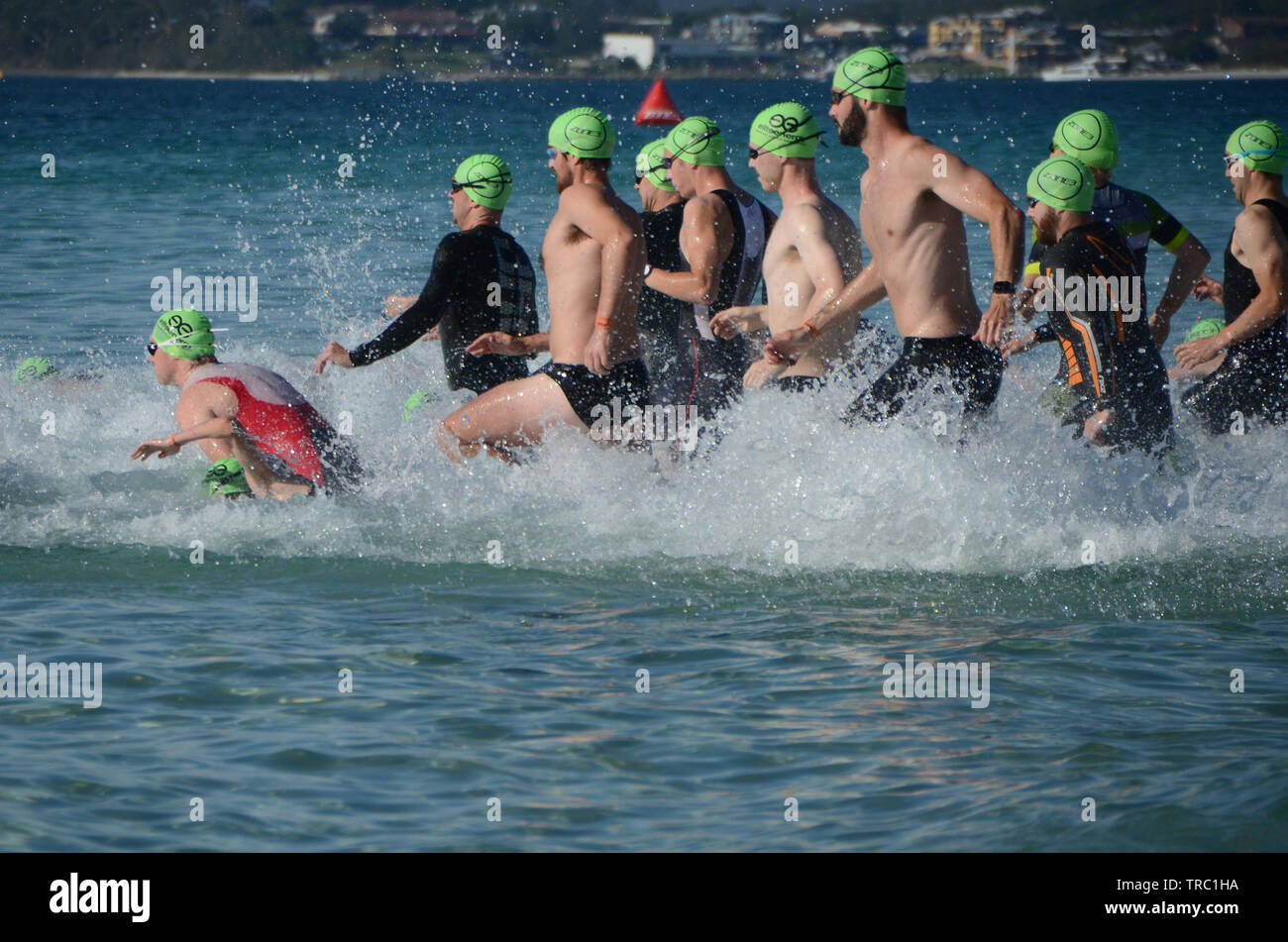 Triatleti maschio eseguire nel surf all inizio della spiaggia Calalla gara di triathlon. I concorrenti in sport di resistenza della gara di triathlon in oceano. Foto Stock