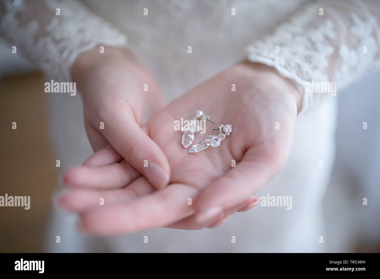 Sposa ottenere pronto per la cerimonia di nozze con focus sulle sue mani tenendo delicatamente una coppia di cristallo argento orecchini a pendente Foto Stock