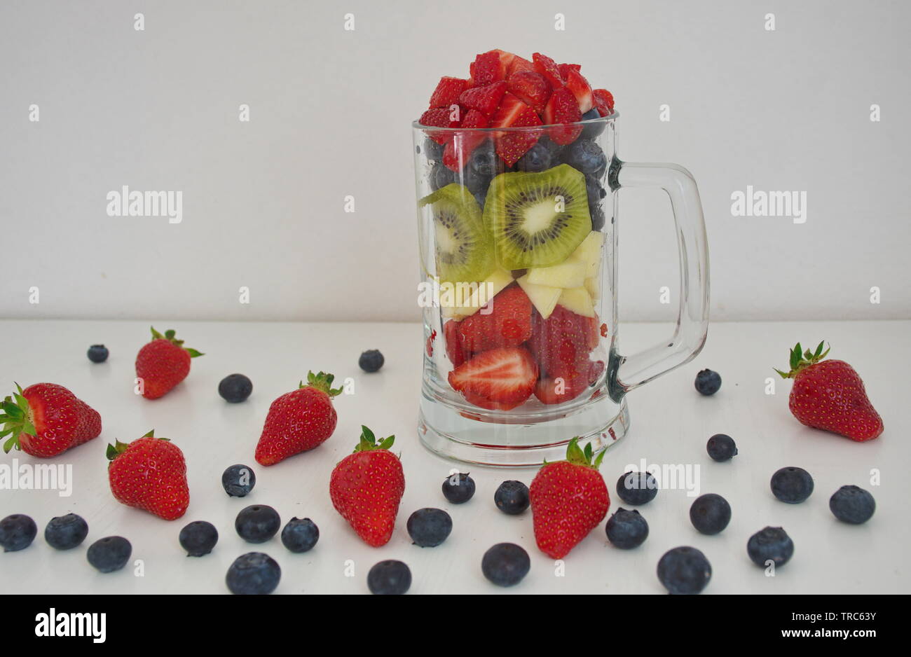 Frutti di bosco, mela e kiwi tagliato e mettere nel bicchiere contro uno sfondo bianco Foto Stock