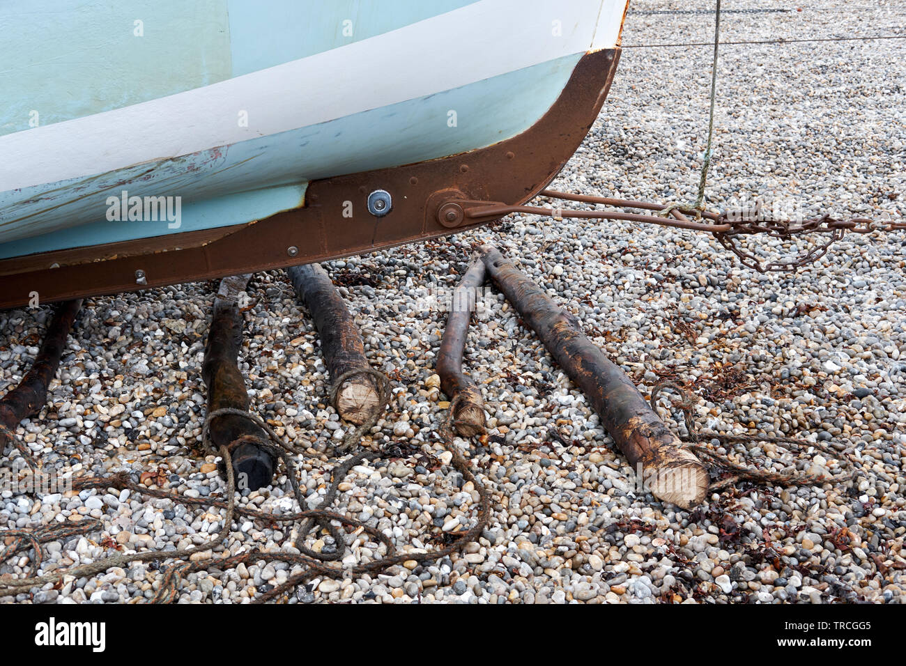 Una barca da pesca viene trasportata su una spiaggia di ciottoli con un argano e rulli di registro Foto Stock