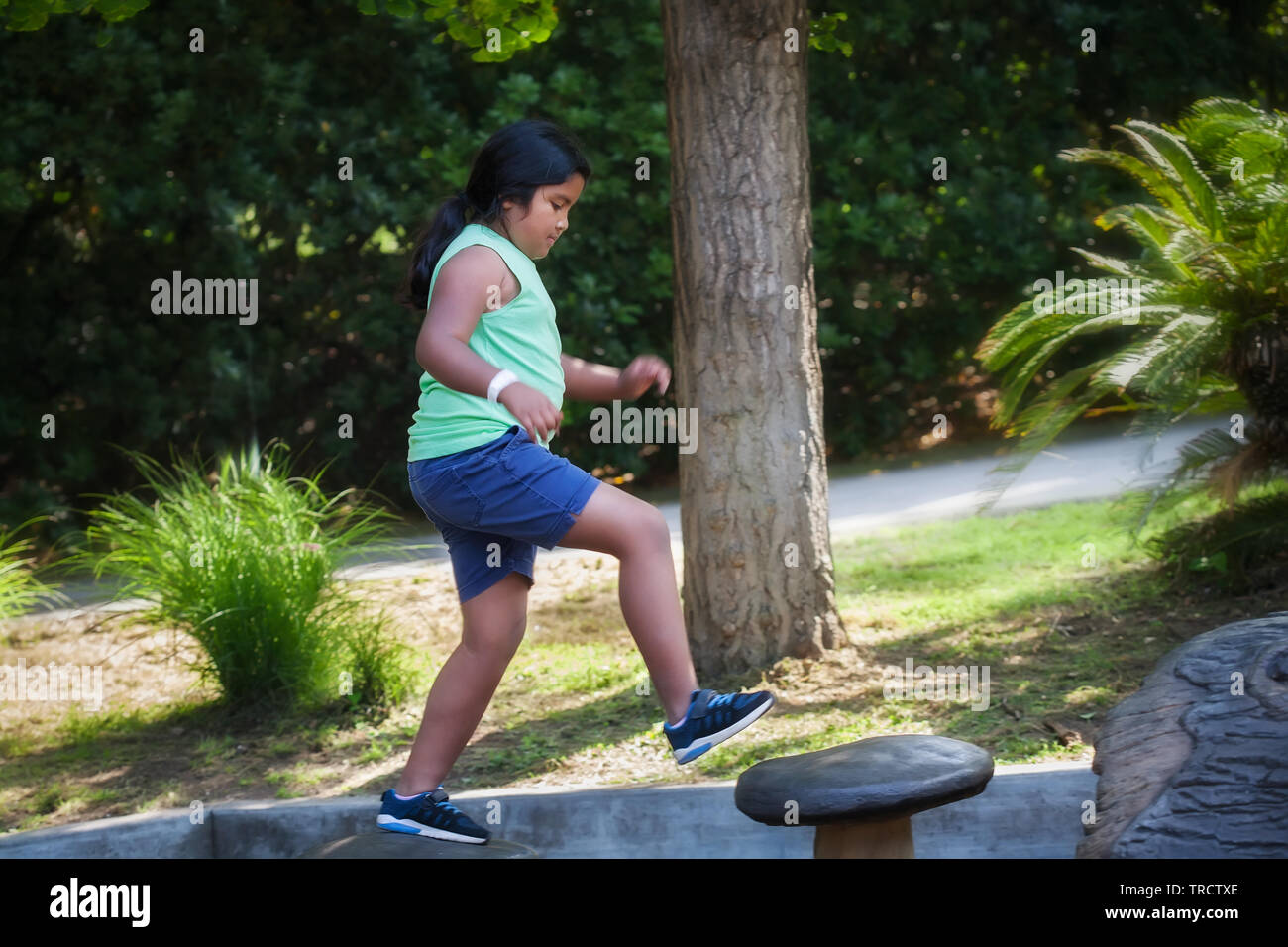 Pre-teen ragazza salta da una fase all'altra in corrispondenza di un parco giochi per bambini, fare attività fisica che si sviluppa il suo senso di equilibrio. Foto Stock