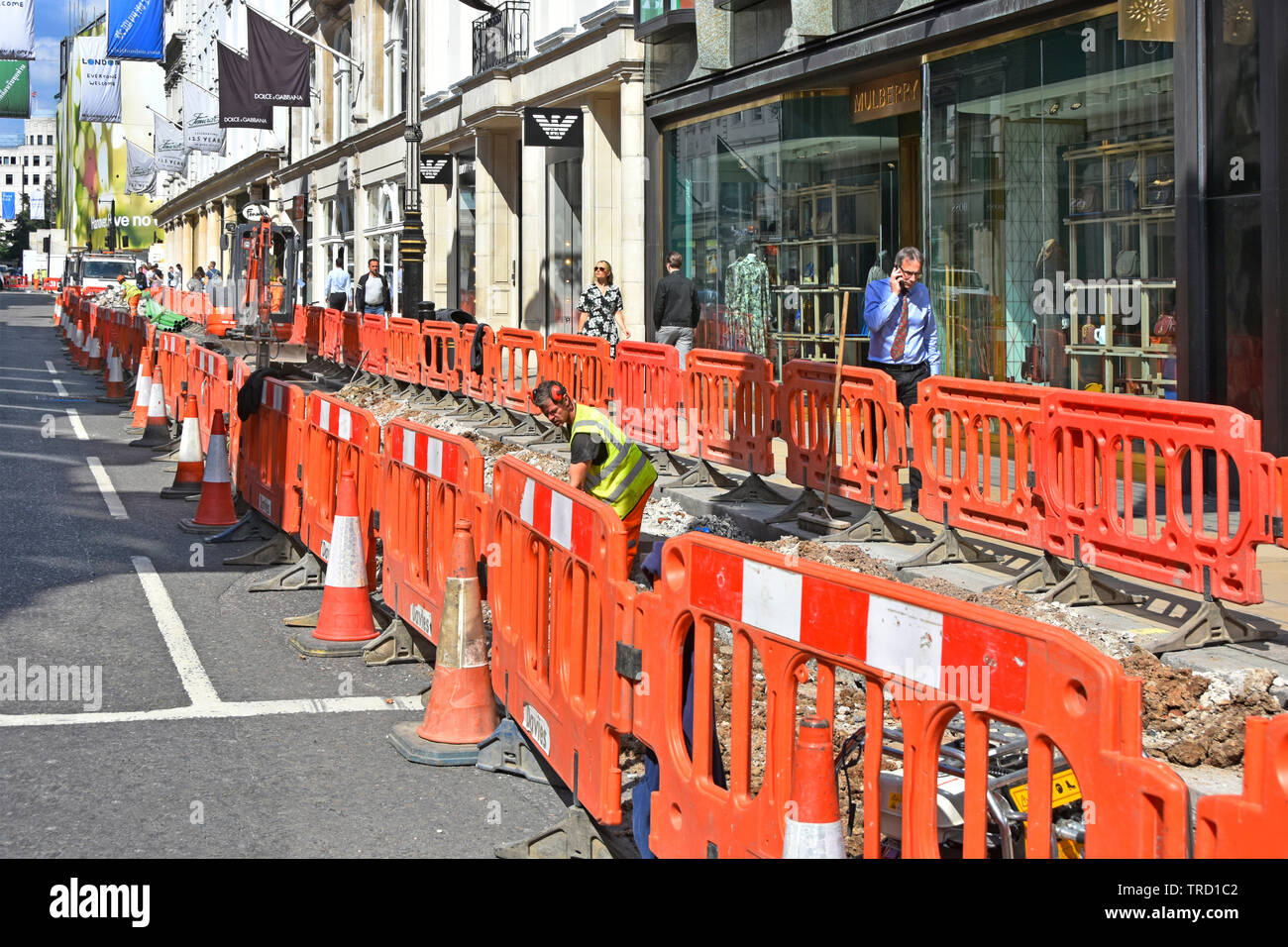 Rosso barriera di plastica & coni che racchiude opere stradali per il contraente e i lavoratori in via cavo di scavo in trincea di strade e vie di Londra West End England Regno Unito Foto Stock