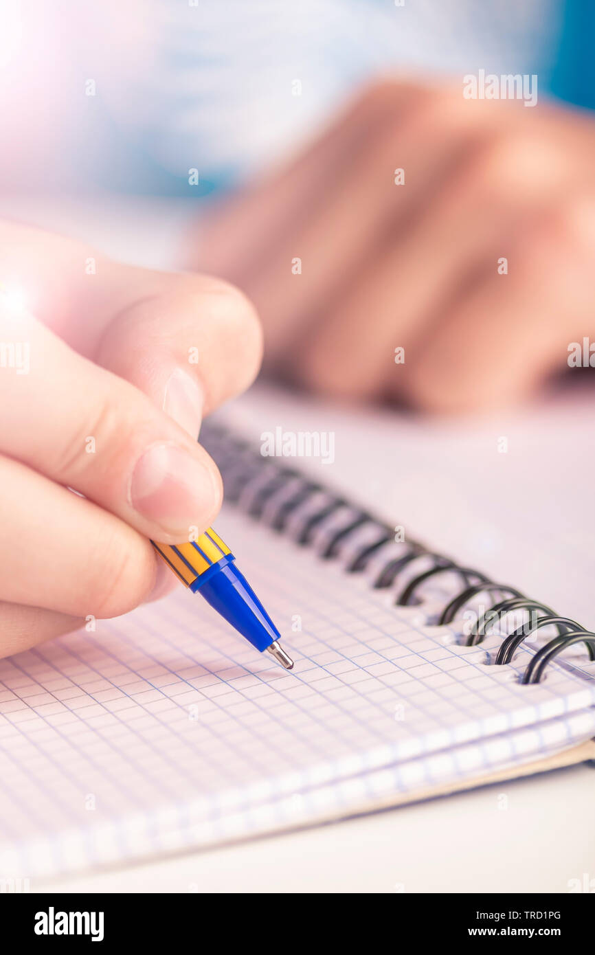 Teen scrive nero giallo penna in un notebook a scacchi. Rilegato a spirale Foto Stock