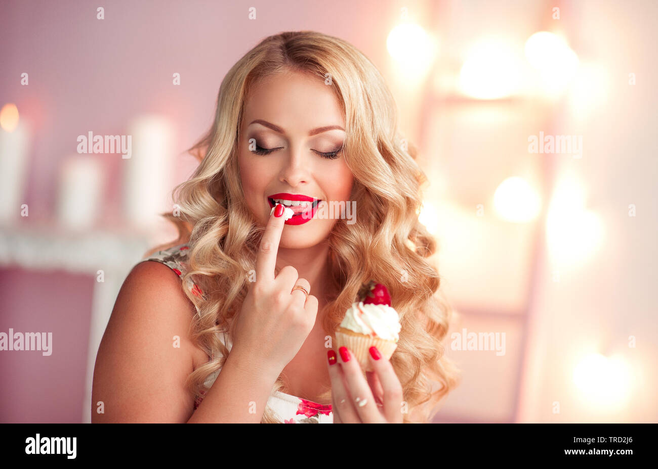 Sorridente donna bionda mangiare cupcake in camera closeup. Toccare la crema con il dito. Foto Stock