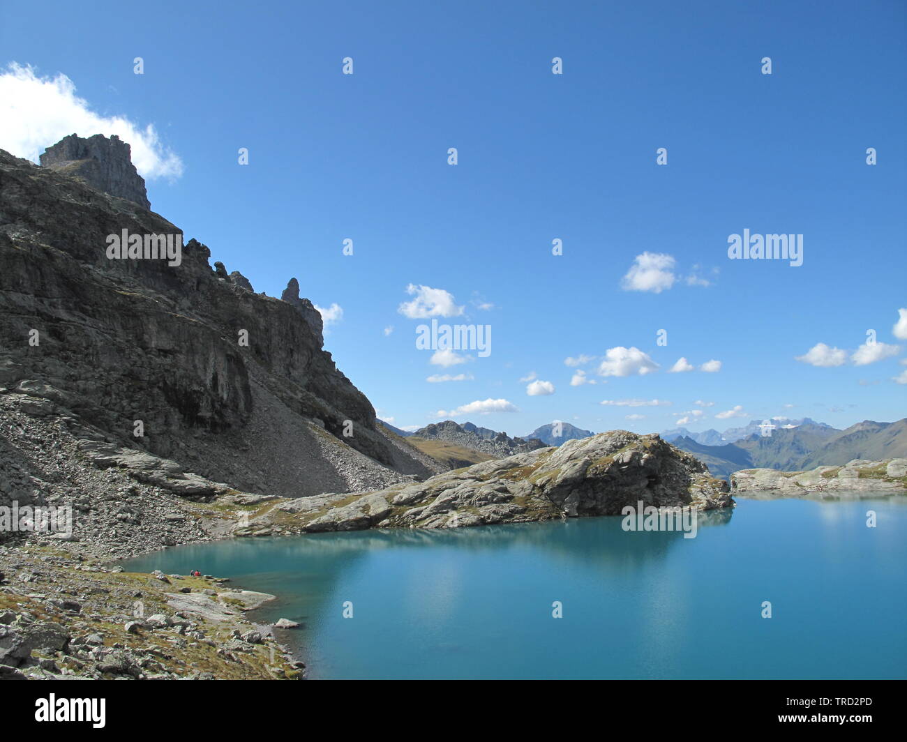 Grigio cime di montagna, cotone nuvole e un profondo cielo blu sono riflesse nella soleggiata turchese del lago alpino Foto Stock