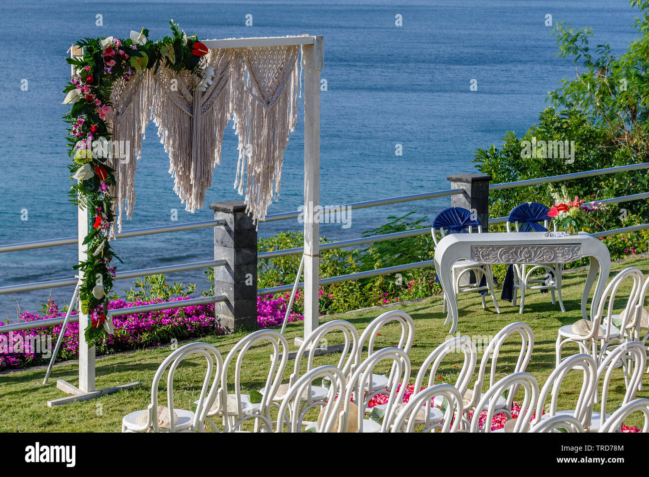 Arco di matrimonio in stile Boho vicino all'oceano decorate con macrame e fiori freschi, sedie, tavolo di firma e petalo corridoio per una cerimonia. Bali. Foto Stock