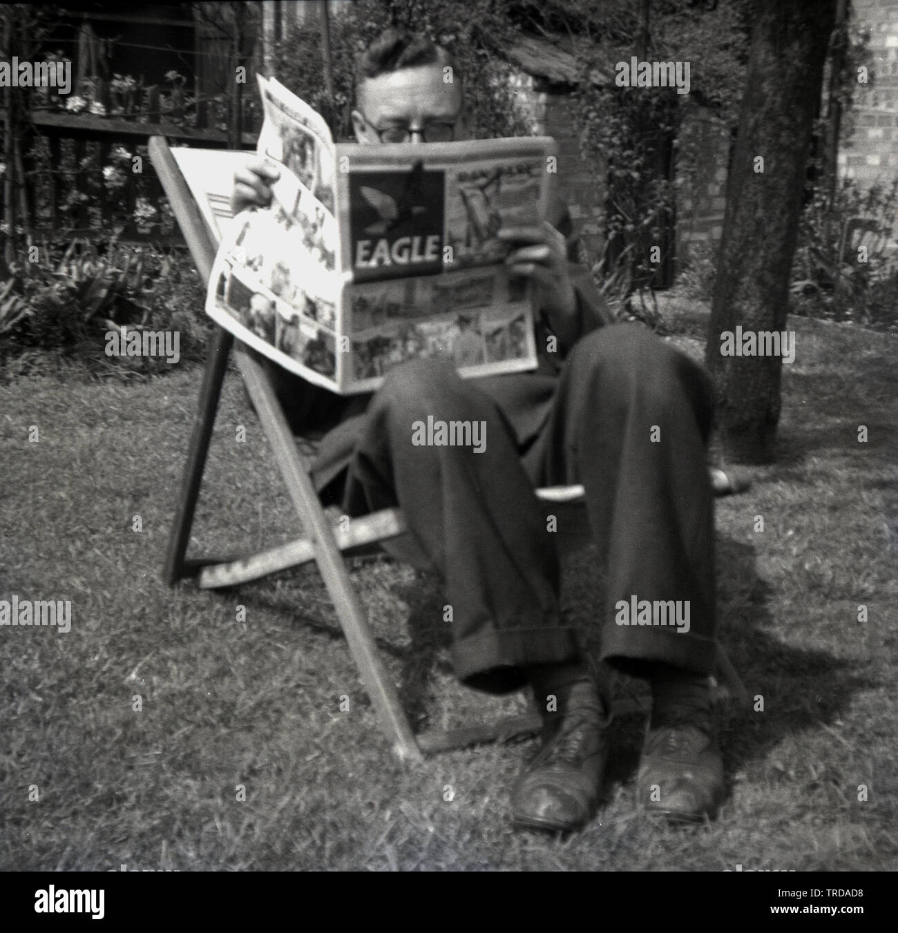 Degli anni Cinquanta, storico, uomo seduto in una sedia a sdraio fuori in un giardino la lettura dell'Aquila, un comic britannico, pubblicato per la prima volta in Inghilterra dal 1950 al 1969, e poi seguendo un rilancio, dal 1982 al 1994. Creato da Marcus Morris e pubblicato da Hulton Press, è stato un enorme successo. Il suo più riconoscibile di carattere è stato Dan osare, pilota del futuro, creato da Frank Hampson. Foto Stock