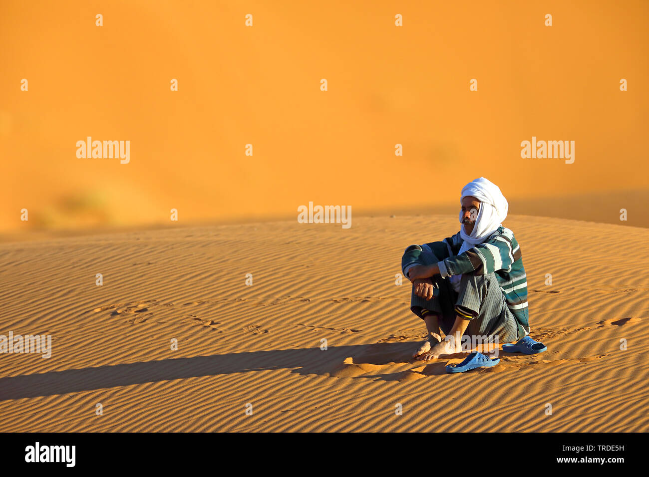 Berber seduta nella sabbia del deserto, Marocco, Merzouga Erg Chebbi Foto Stock