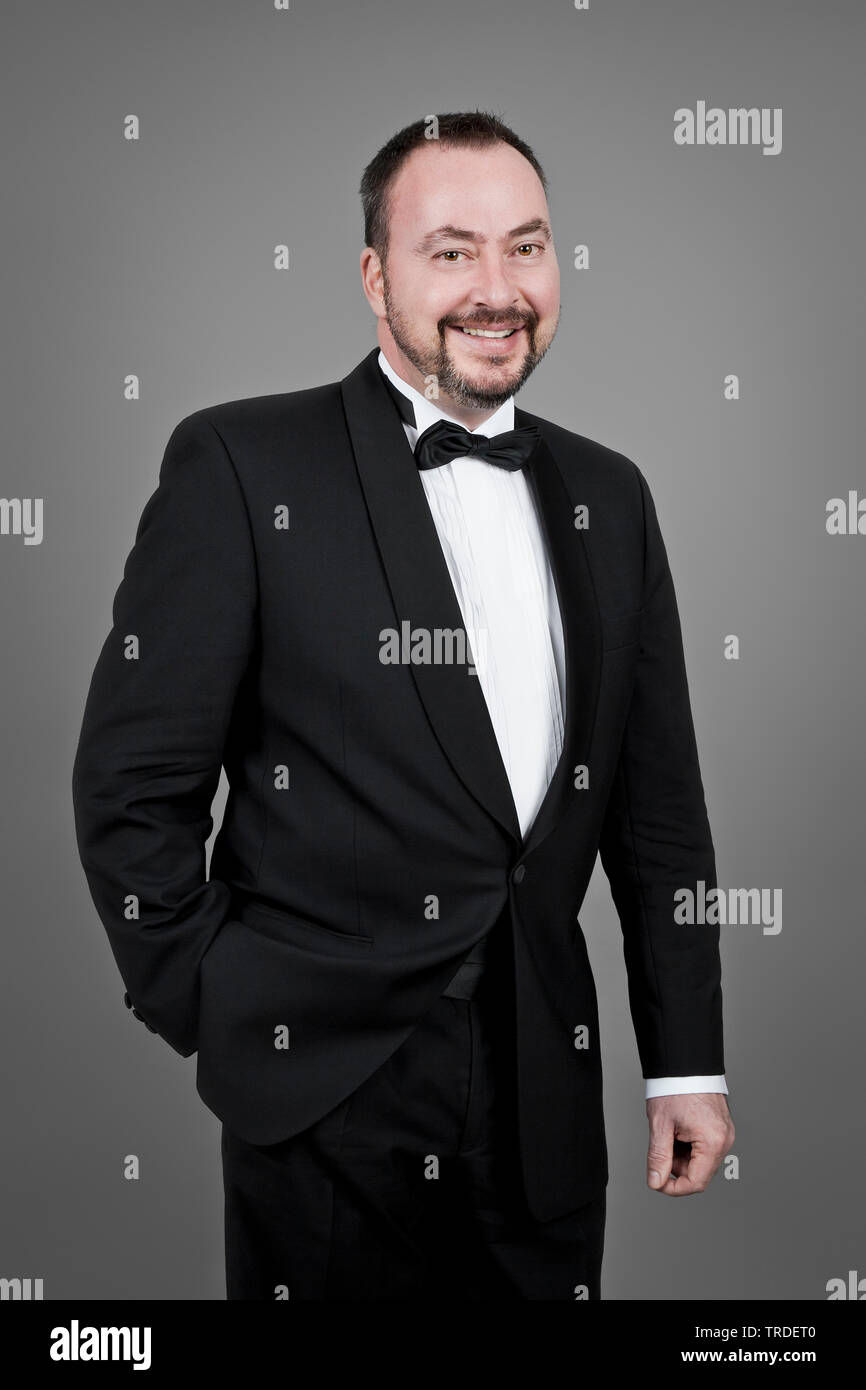 Ritratto di una buona ricerca e sorridente uomo vestito in una camera fumatori contro uno sfondo grigio Foto Stock